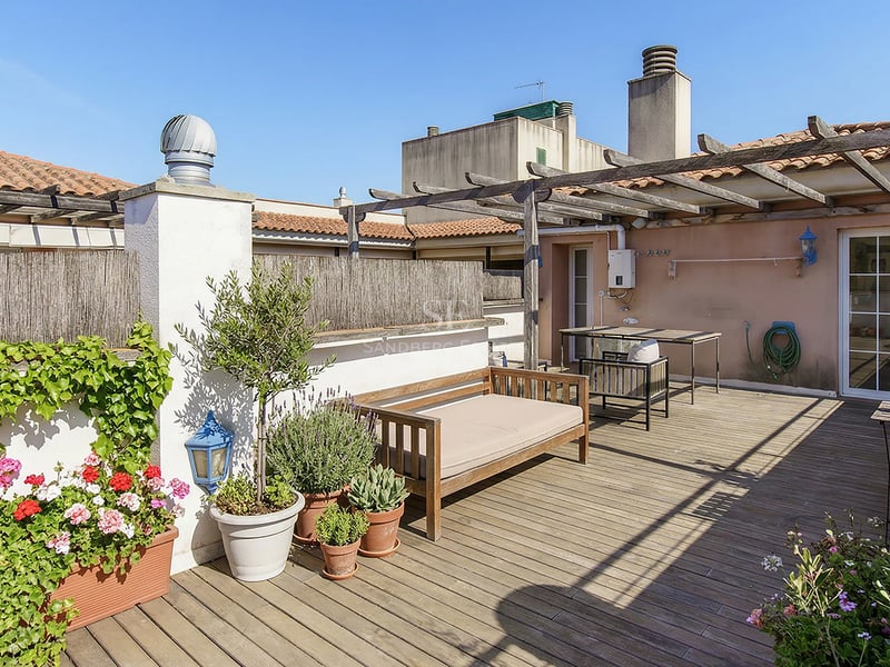 Solig takterrass med trädäck, pergola, blomkrukor och utemöbler för avkoppling.