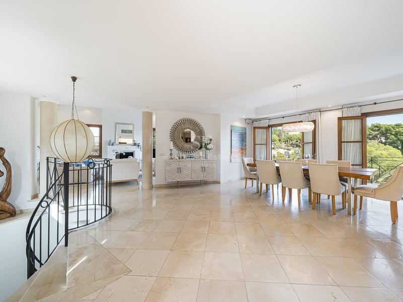 Rymlig matsal med beige marmorgolv, träbord och naturligt ljusinsläpp från stora dörrar.