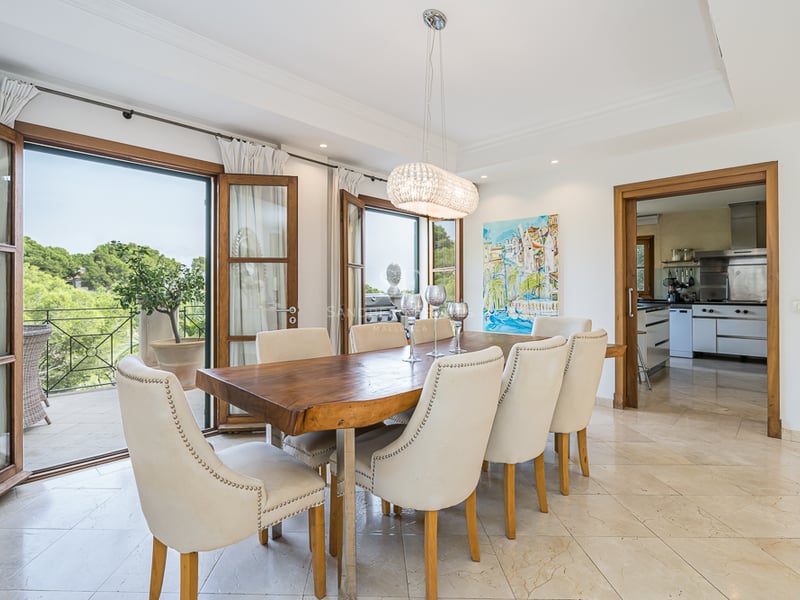 Matsal med ett massivt träbord, krämvita stolar och stora glasdörrar som leder ut till en balkong.