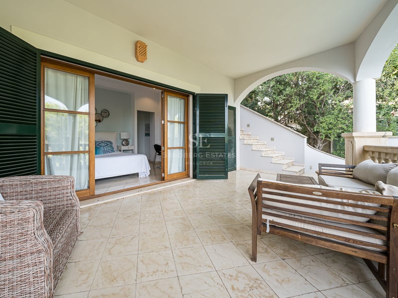 Övertäckt medelhavsterrass med klinkergolv, trämöbler och stora skjutdörrar som leder till ett sovrum.