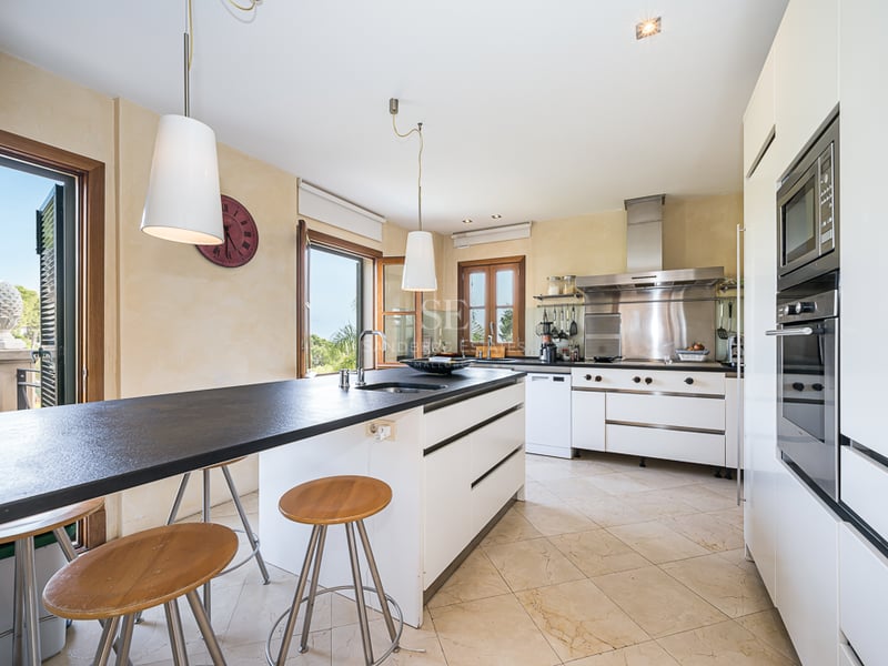 Modernt kök med mörk köksö, barstolar i trä, mörk bänkskiva och vitvaror i rostfritt stål.