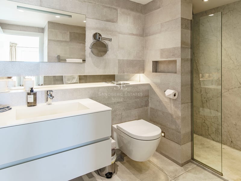 Minimalist bathroom featuring grey stone walls, white floating vanity, and a glass walk-in shower.