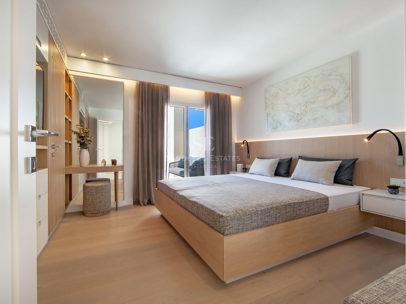 Chambre de maître moderne avec lit en bois, éclairage intégré et accès à un balcon ensoleillé.