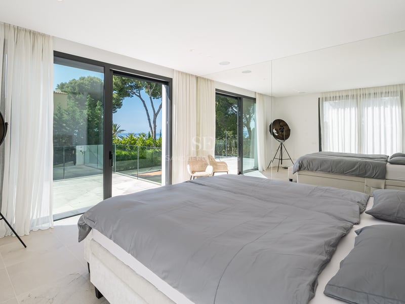 Chambre moderne avec grand lit, baies vitrées et terrasse privée offrant une vue sur les pins et la mer.