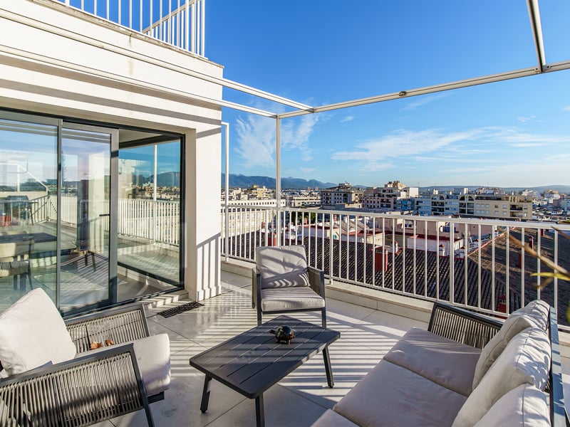 Grande terrasse blanche avec canapé et fauteuils d'extérieur modernes surplombant la ville et les montagnes.