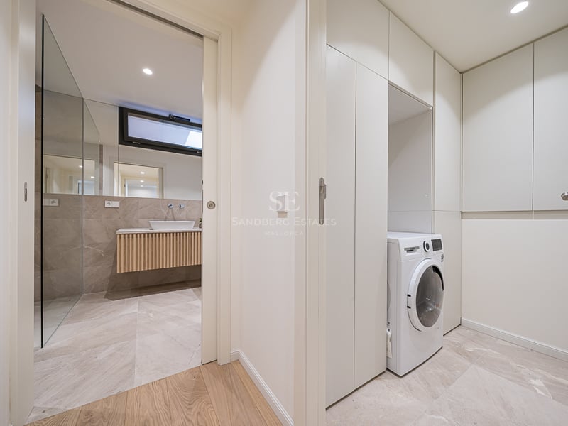 A clean utility room with a white washing machine and built-in cupboards next to a modern stone bathroom with a vessel sink.