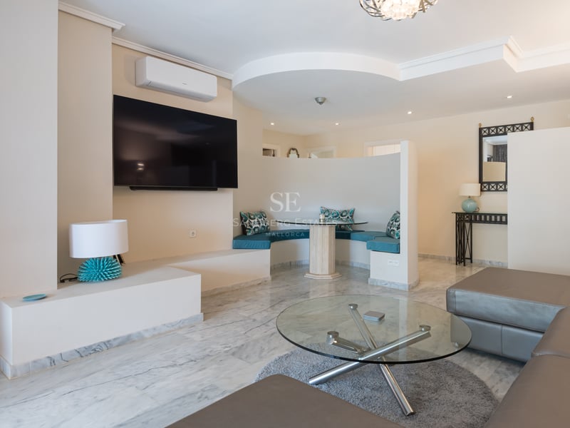 Modern living room featuring marble floors, a large TV, leather sofa, and a curved breakfast nook with turquoise cushions.