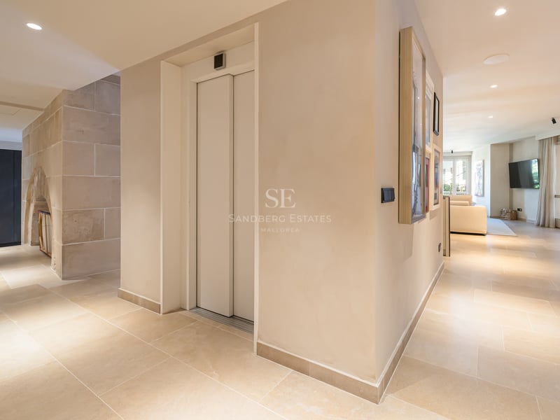 Couloir intérieur moderne avec ascenseur privé blanc, sol en pierre naturelle et éclairage encastré chaleureux.