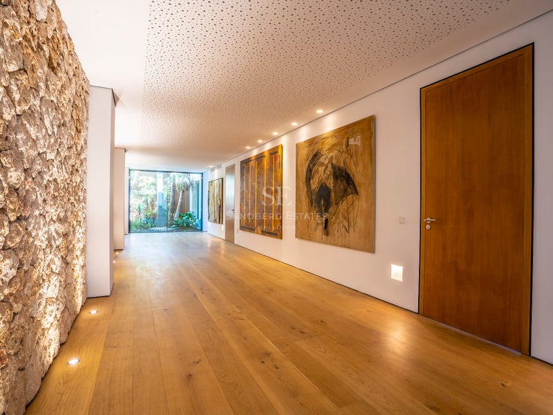 Langer moderner Flur mit Eichendielen, weißen Wänden mit Kunstwerken und Glastür zum Garten am Ende.