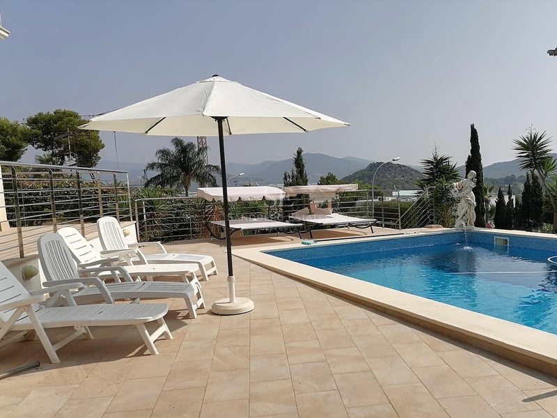 Espace piscine ensoleillé avec chaises longues blanches, parasol et statue décorative surplombant les montagnes.