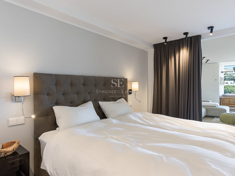 Modernes Hauptschlafzimmer mit grauem gestepptem Kopfteil, weißer Bettwäsche und Glastüren zum Balkon.