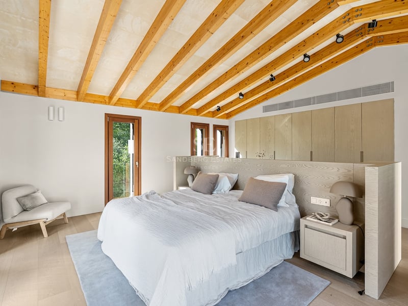 Chambre principale moderne avec plafond incliné, poutres en bois, grand lit et placards intégrés.
