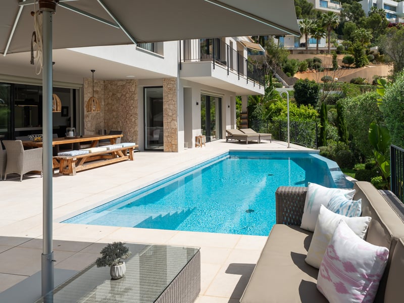 Vue panoramique de piscine à débordement, entourée de végétation et d'architecture moderne. Lumière naturelle et ambiance sereine.