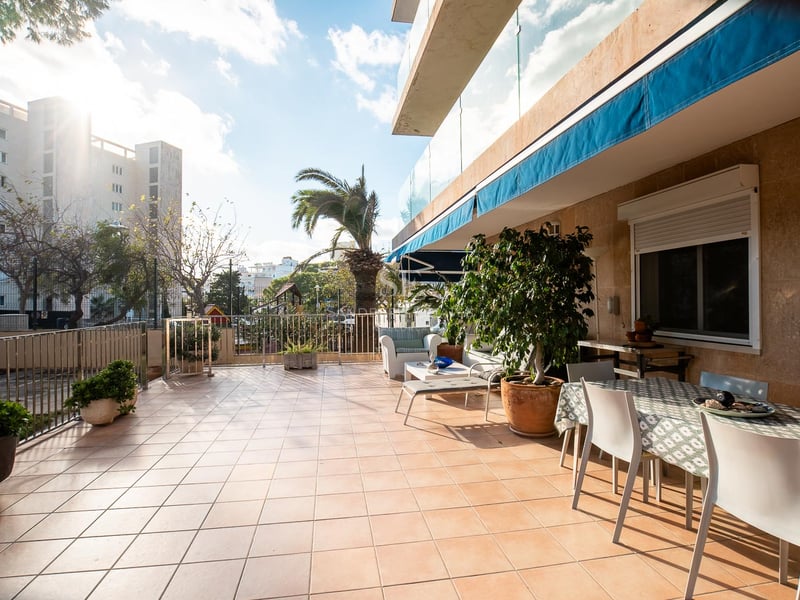 Große Außenterrasse mit Terrakottafliesen, Esstisch, Loungemöbeln und blauen Markisen bei strahlendem Sonnenschein.