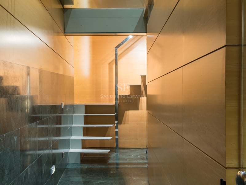 Couloir intérieur moderne avec murs en panneaux de bois clair, sol en pierre sombre polie et escalier blanc flottant.