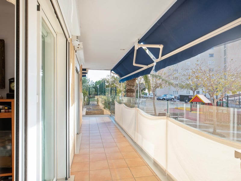 Langer Balkon mit Terrakottafliesen, Glasgeländer und blauen Markisen mit Blick auf die Wohngegend.