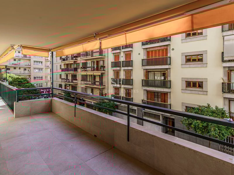 Large terrasse en pierre avec garde-corps métallique et stores orange donnant sur des immeubles résidentiels.