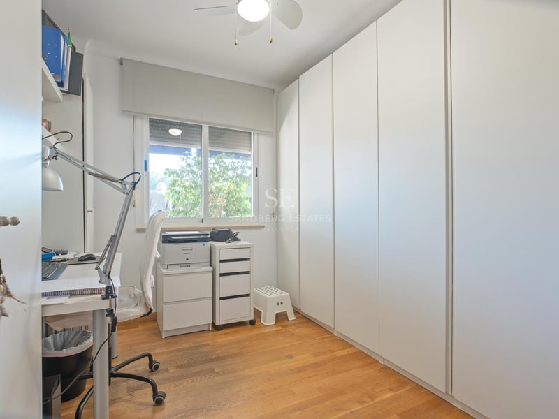 Heller Raum mit deckenhohen weißen Einbauschränken, Holzboden und einem Schreibtisch am Fenster.