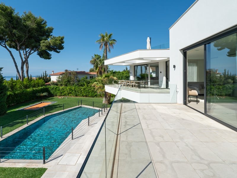 Vue surélevée depuis une terrasse moderne blanche sur une piscine rectangulaire, une pelouse et des pins.