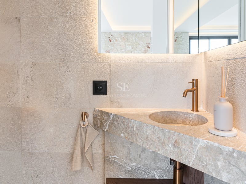 Nahaufnahme eines integrierten Natursteinwaschbeckens mit gebürsteter Messingarmatur und hinterleuchtetem Spiegel.