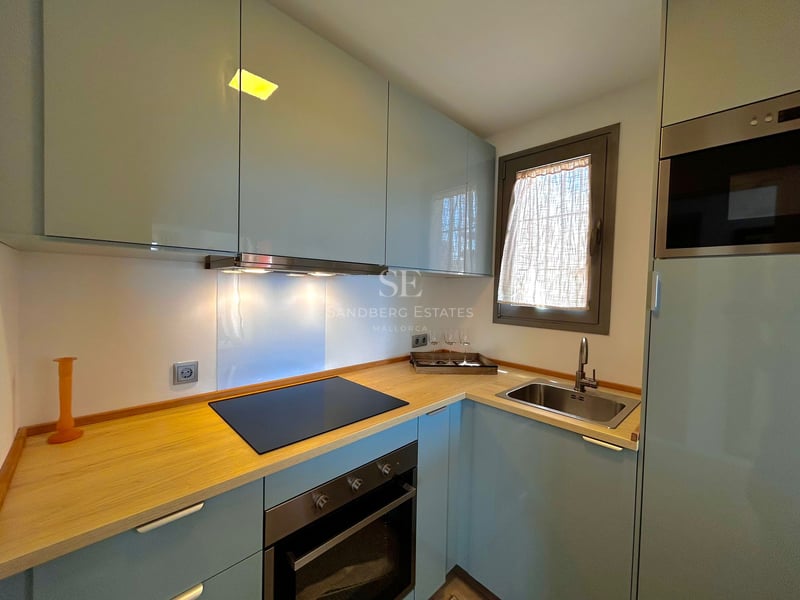 Modern kitchen featuring glossy light blue cabinets, light wood countertops, induction hob, and stainless steel sink.