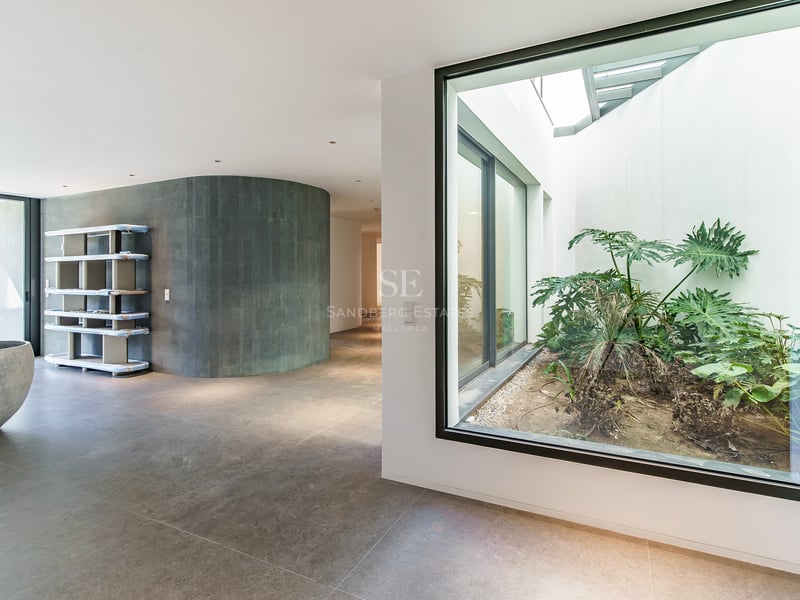 Couloir moderne avec un mur courbe en pierre grise et une grande fenêtre donnant sur un patio intérieur avec des plantes.
