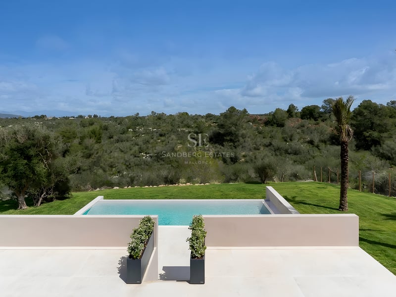 Rechteckiger Infinity-Pool mit heller Steinterrasse und Blick auf die grünen mediterranen Hügel.