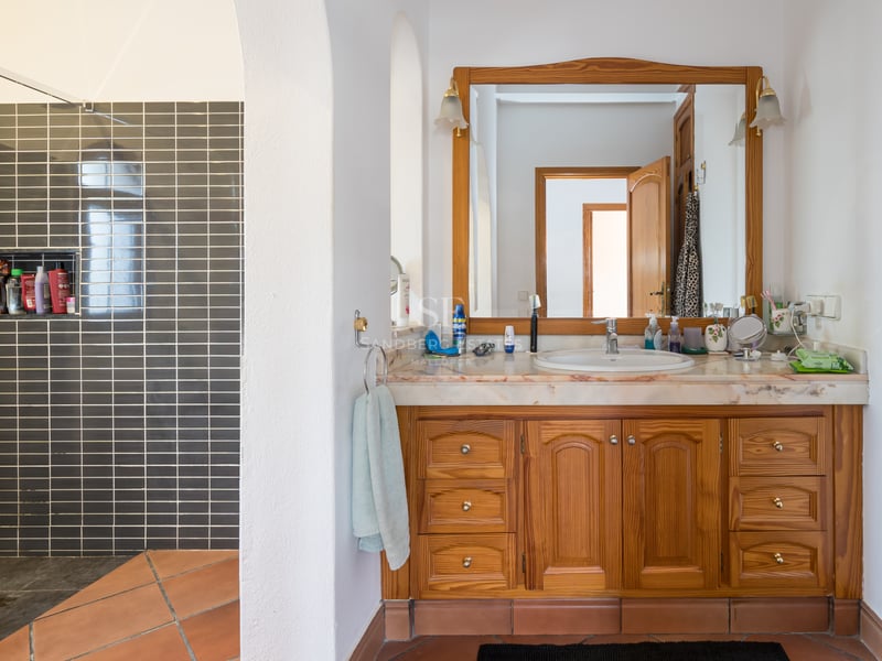 Bathroom featuring a wooden vanity with marble top, terracotta floor tiles, and a walk-in shower with dark grey tiles.