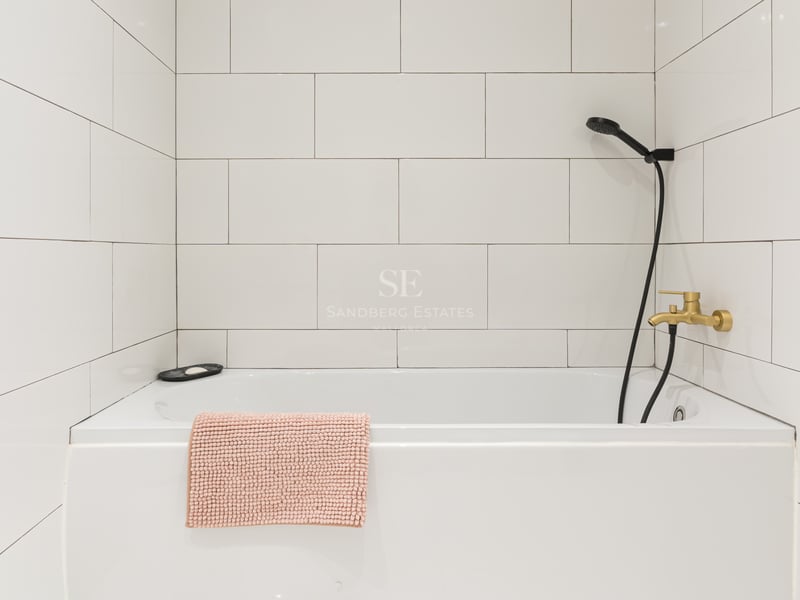 Baignoire blanche, carrelage mural, robinetterie dorée et pommeau de douche noir.