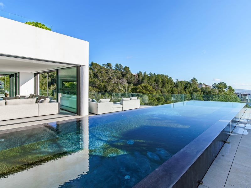 Villa de luxe avec piscine à débordement, terrasse vitrée et salon moderne surplombant une forêt.