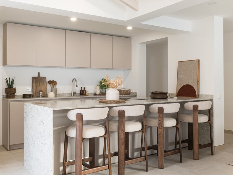 Cuisine contemporaine avec placards beiges, îlot en pierre blanche et quatre tabourets en bois et tissu.