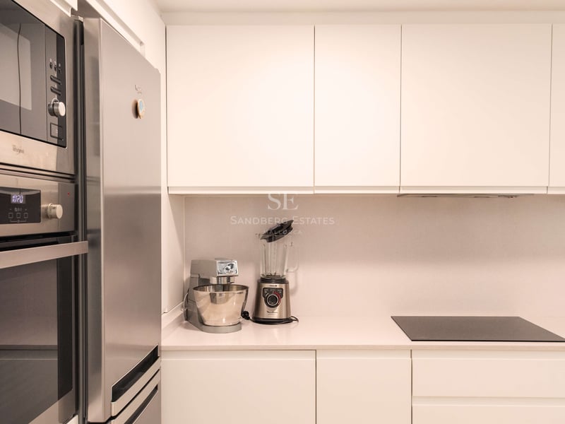 Weiße minimalistische Küche mit Edelstahlgeräten, Steinarbeitsplatte und grifflosen Schränken.