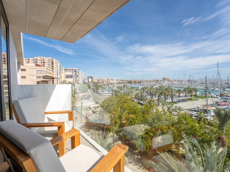 Modern balkong med träfåtöljer och glasräcke med panoramautsikt över en marina och staden.