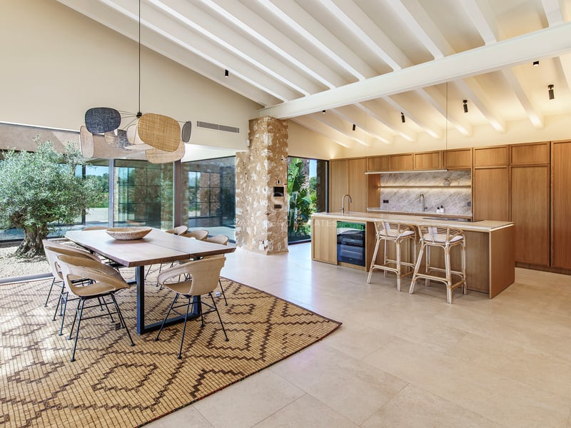 Offene Designerküche mit Holzelementen, Essplatz, weißen Deckenbalken und Natursteinwand.