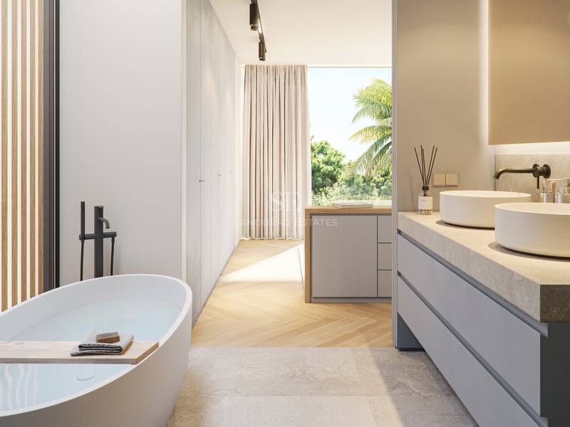 Minimalist bathroom with a freestanding tub, oak herringbone floors, and floor-to-ceiling windows overlooking palm trees.