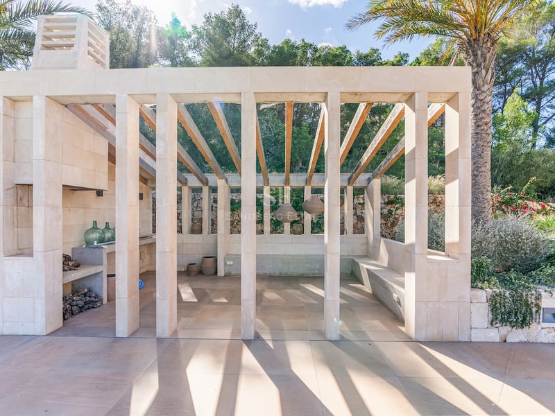 Pavillon moderne en pierre avec poutres en bois, cheminée extérieure et banquettes intégrées entouré de palmiers.