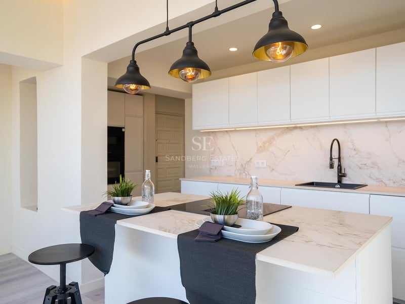 Moderne weiße Küche mit Marmor-Arbeitsplatte und drei schwarzen Industrie-Pendelleuchten.