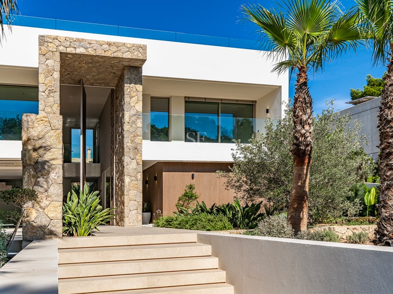 Entrée de villa moderne avec de larges marches en pierre, un haut portail en pierre et des palmiers.
