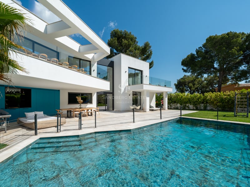 Extérieur de villa contemporaine blanche avec piscine, clôture de sécurité et terrasse couverte avec coin repas.