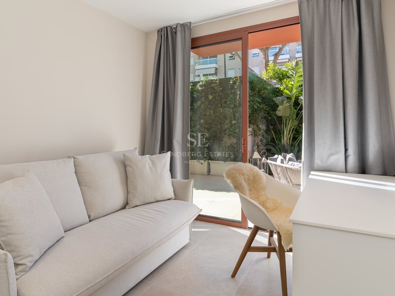 Bright modern room featuring a cream sofa, white desk, and large sliding doors leading to a green private patio.