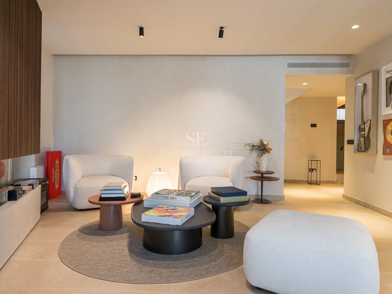 Espace lounge moderne avec fauteuils blancs, tables basses anthracite et mur en tasseaux de bois avec cheminée.