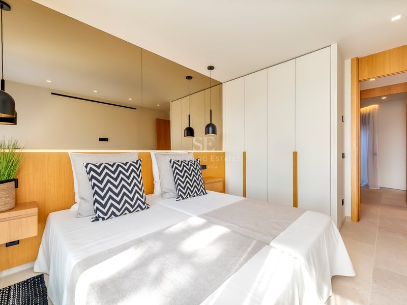 Chambre contemporaine avec tête de lit en bois, mur de miroirs et grands placards blancs intégrés.