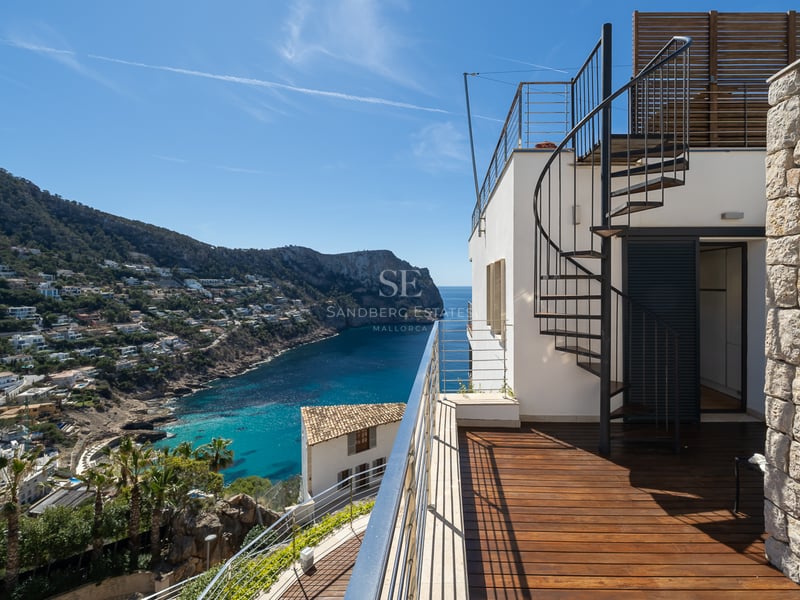 Terrace with wooden decking and a spiral staircase overlooking a Mediterranean bay and mountains.