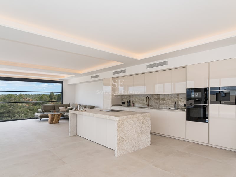 Minimalistische weiße Küche mit großer Marmorinsel, integrierten Geräten und indirekter Deckenbeleuchtung.