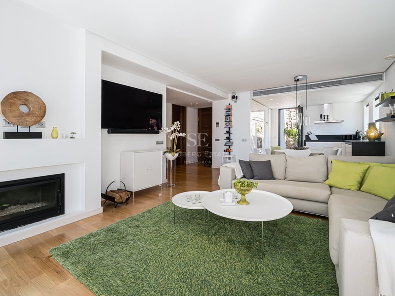 Bright living room with wood floors, L-shaped sofa, modern built-in fireplace, and green rug in an open layout.