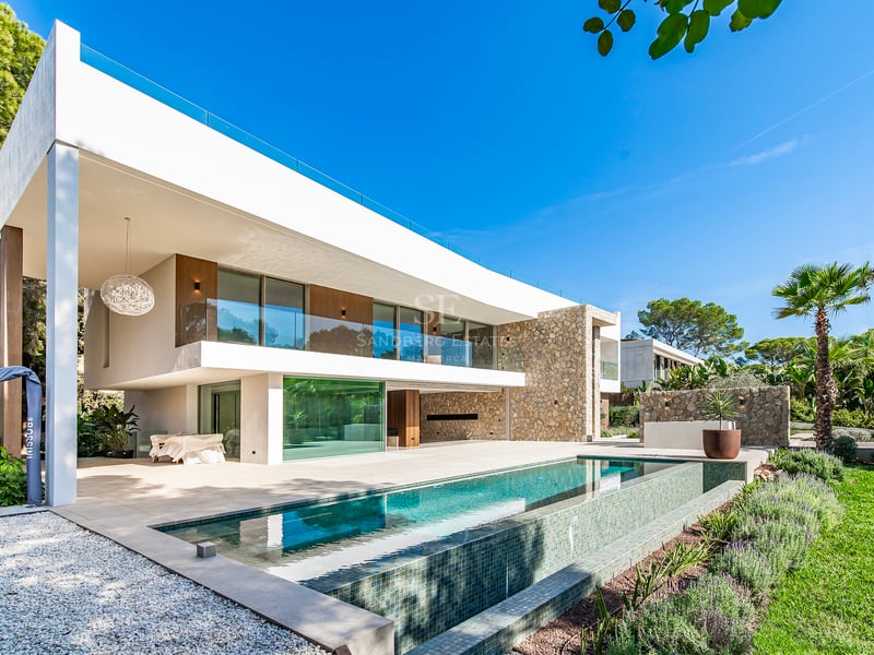 Façade de villa moderne avec piscine à débordement, murs en pierre naturelle et grandes baies vitrées.