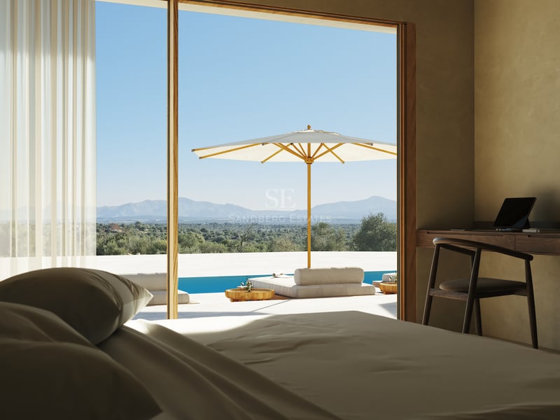 Chambre avec bureau en bois et grandes baies vitrées ouvrant sur une terrasse avec piscine et vue sur les montagnes.