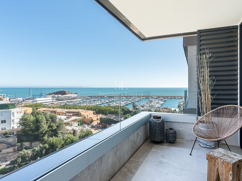 Moderner Balkon mit Glasgeländer und Blick auf einen Yachthafen und das Mittelmeer unter blauem Himmel.