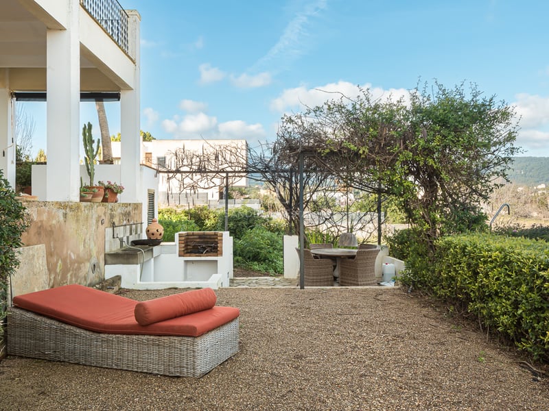 Terrass med orange solstol, inbyggd grill och matplats under en grönskande pergola.