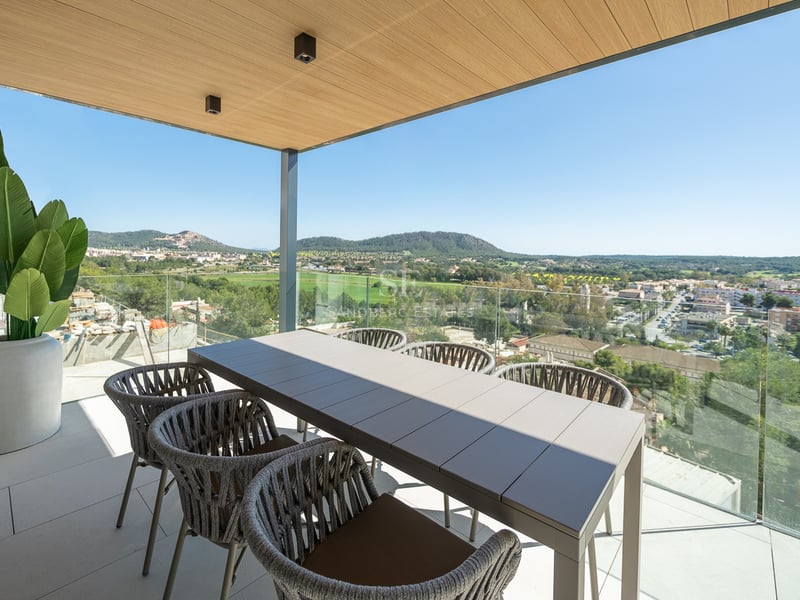 Terrasse couverte contemporaine avec table à manger pour six, garde-corps en verre et vue sur un village méditerranéen.